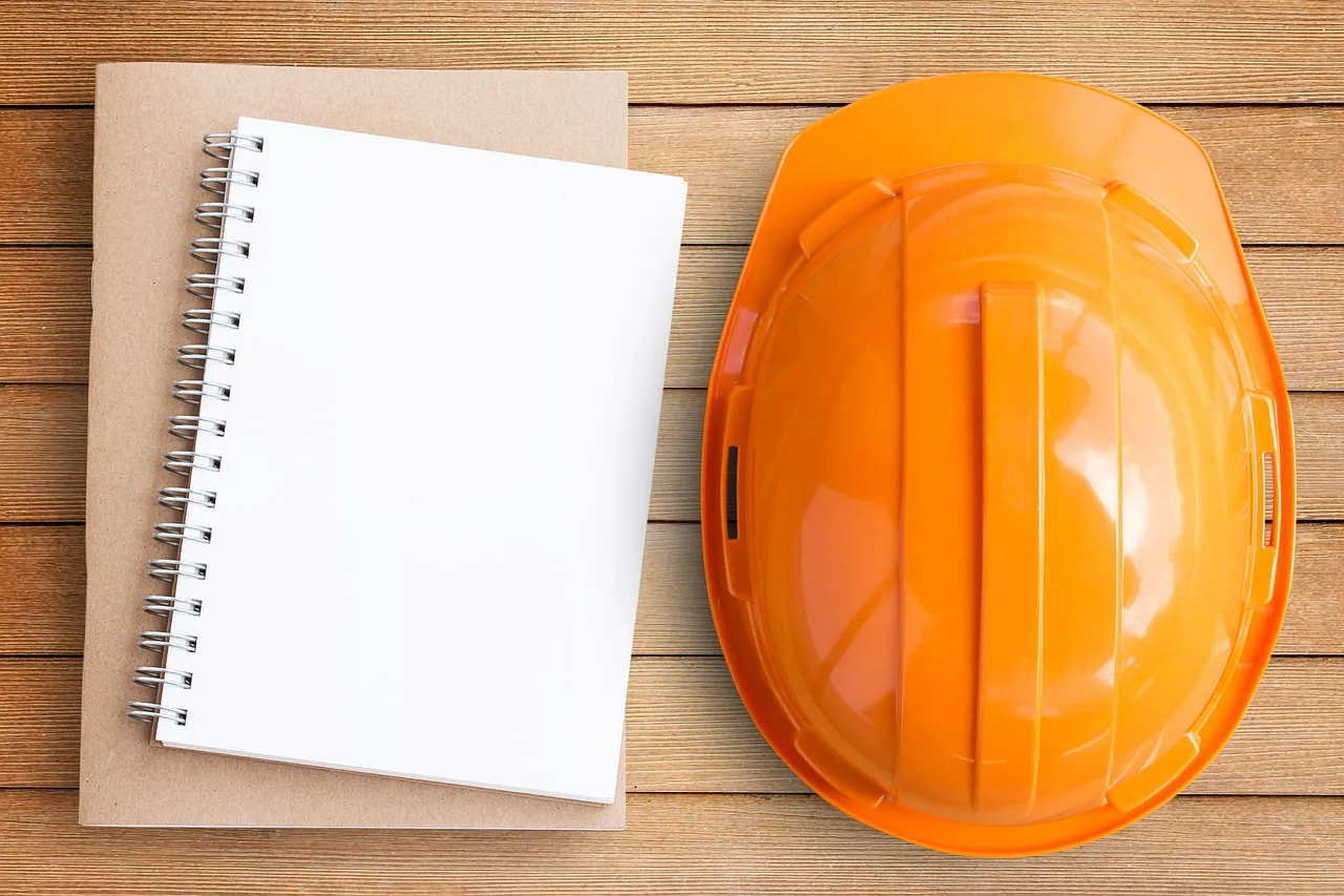 Orange hard hat and blank notebook on a wooden surface.