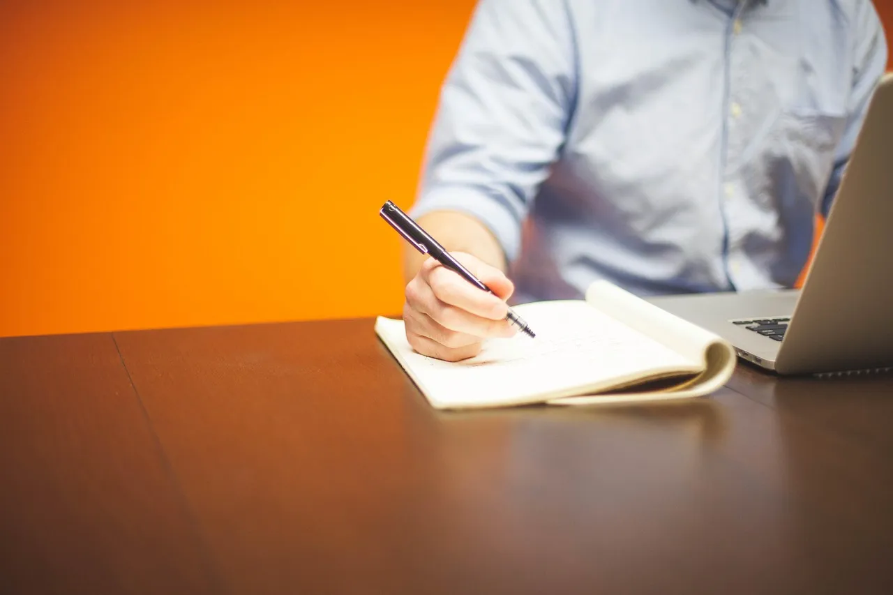 Person writing in a notebook next to a laptop, possibly for BIM coordination planning.