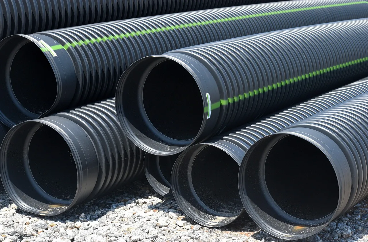 Black corrugated drainage pipes stacked on gravel. Water utilities infrastructure.