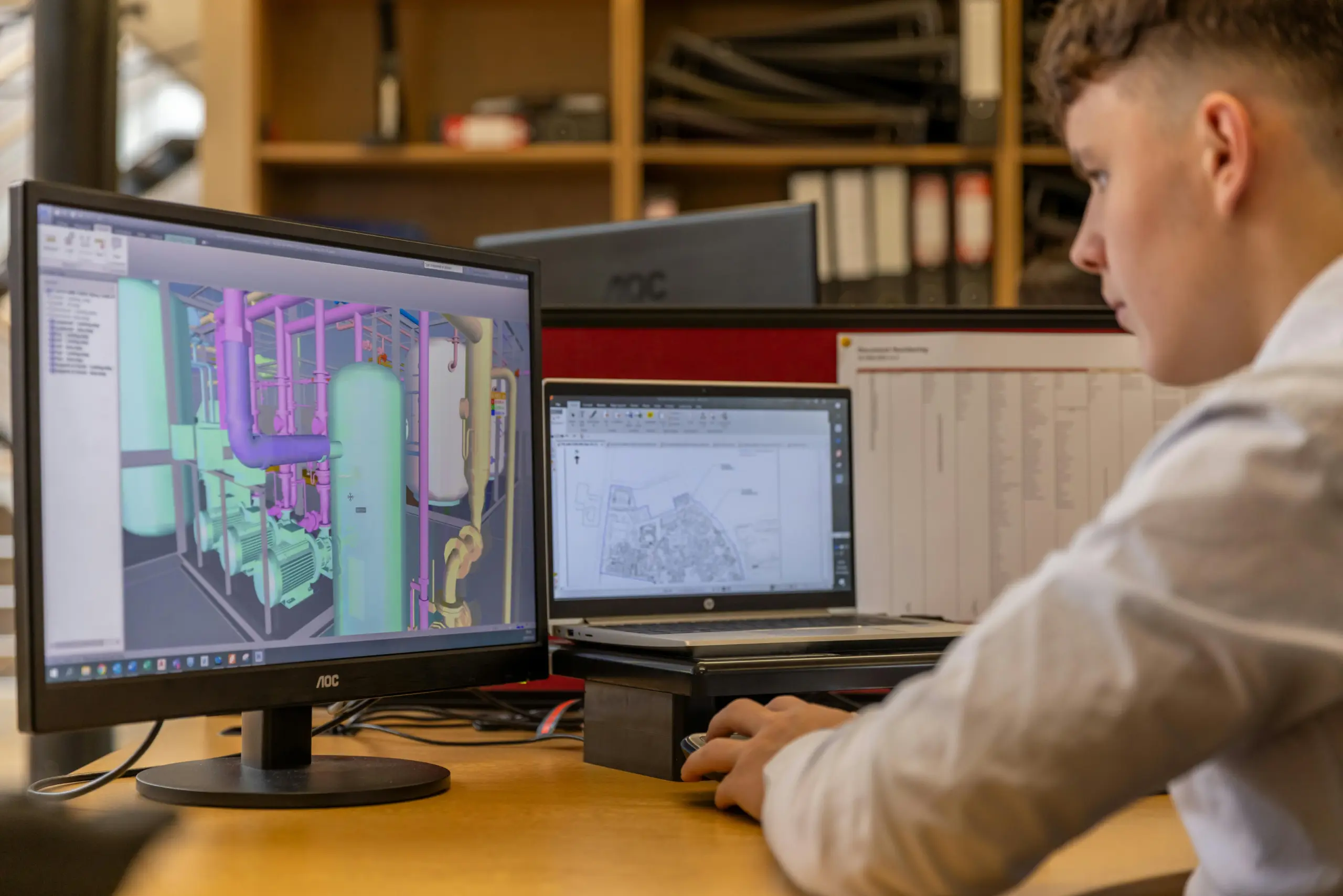 Man viewing a 4D BIM construction sequencing model on a computer screen, showcasing a detailed 3D industrial design.