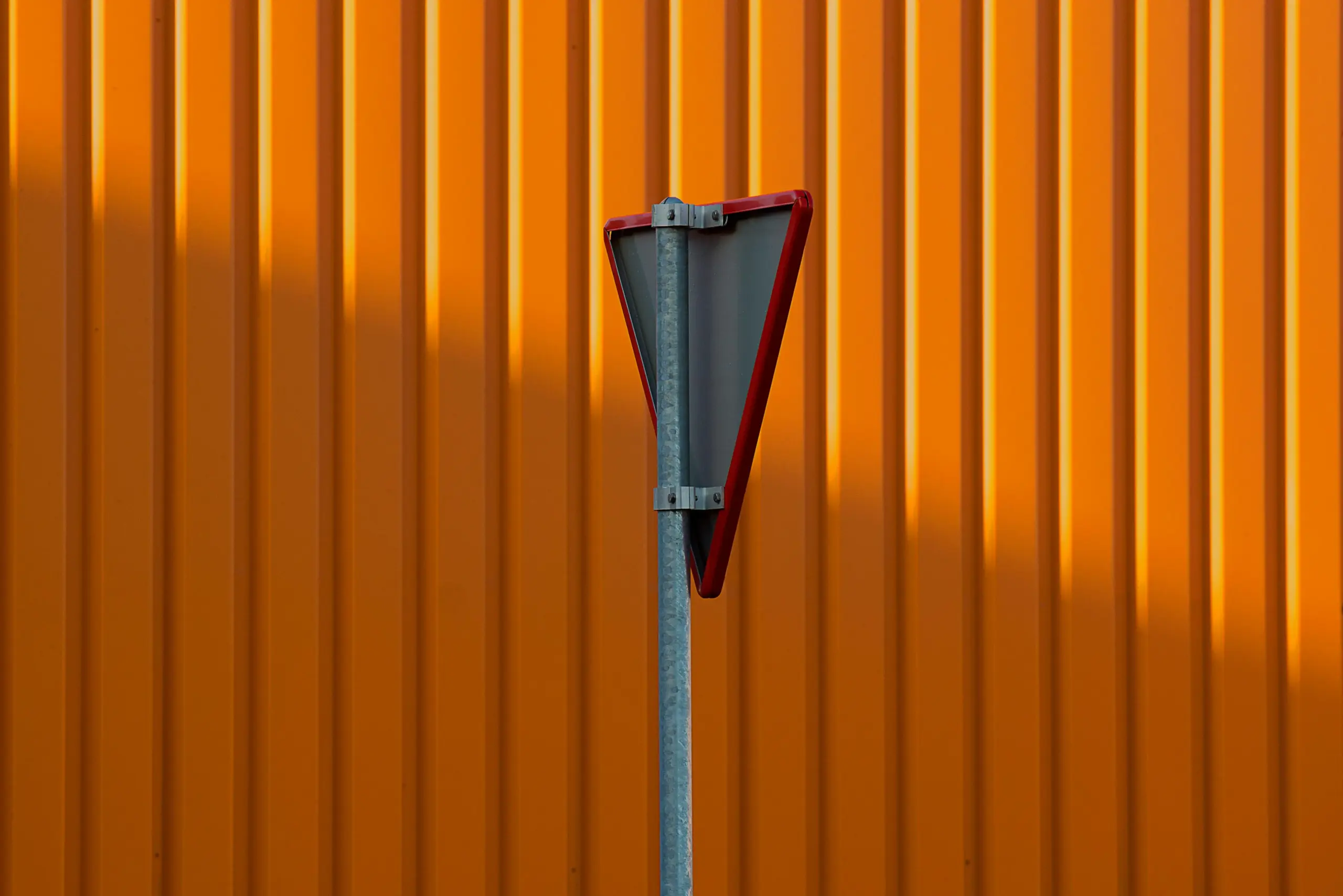 Yield sign against an orange corrugated metal wall, relevant to road junction infrastructure.