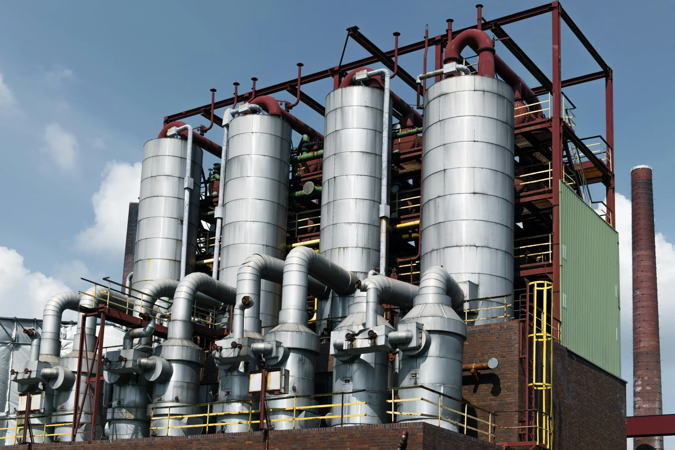 Industrial plant with silver tanks and red piping against a blue sky.